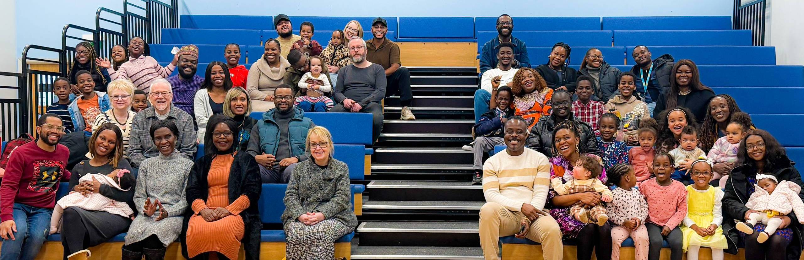 A picture showing a group of multi-ethnic church sitting on tiered seating going back 5 rows.